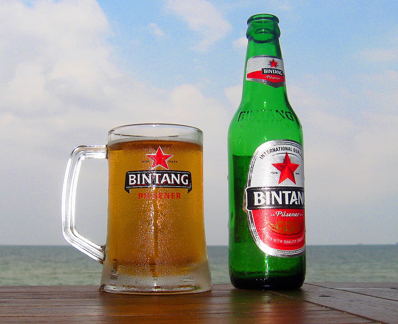 A glass and a bottle of Bintang beer by the beach