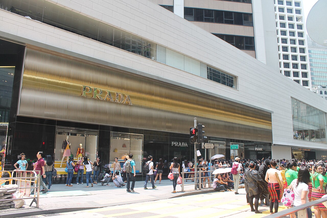 Prada storefront in Hong Kong, with a gold facade and pedestrians on the street.