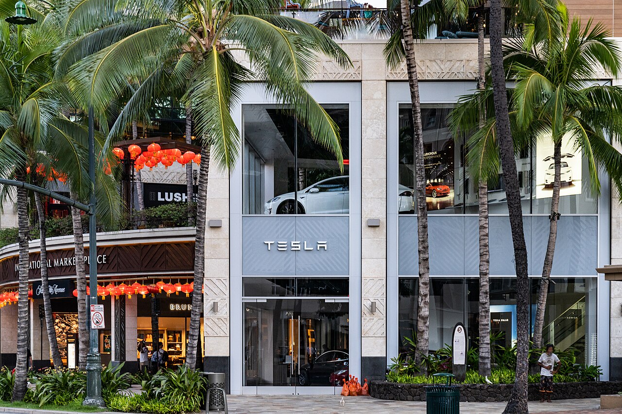 Tesla store front in Honolulu with the Tesla name above the glass entrance and a car inside
